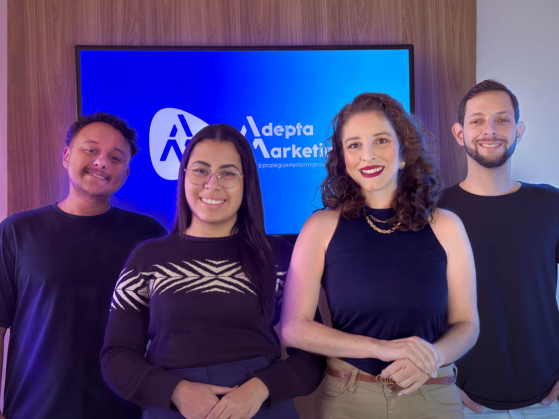Equipe da Adepta Marketing reunida em frente à identidade visual da empresa.